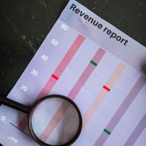 A magnifying glass on a vertical bar chart titled "Revenue report" showing monthly data analysis.